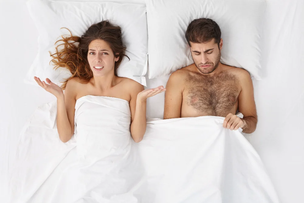 O que é Disfunção Erétil e quais os tratamentos? 3 indoor shot upset female bed shrugging shoulders confusion worrying about her husband who is suffering from impotence