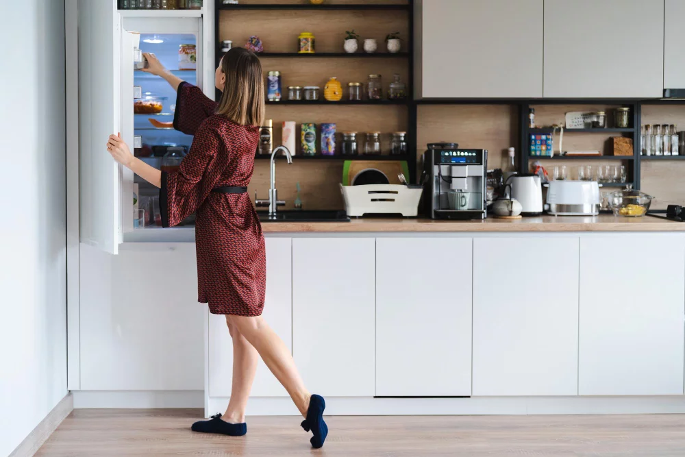 Decoração de Cozinha Simples: Como fazer? 3 mulher com fome procurando comida na geladeira em casa mas nao tem muito la moveis de cozinha brancos em casa usam roupao de seda vermelho